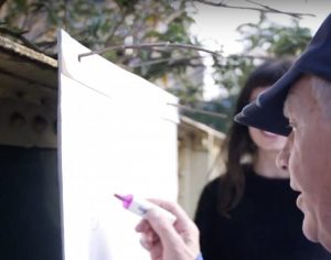A large pad of drawing paper is attached to strong twigs coming from a bush by the street.